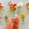 A hand holds a small glass jar filled with pink and red flowers, labeled Good Luck, against a blurred background of similar f