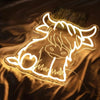 A glowing neon sign shaped like a highland cow is displayed on a dark fabric background.
