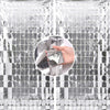 A hand is touching a silver sequin glitter party backdrop made of reflective tiles.