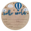 A wooden birth announcement plaque featuring a blue hot air balloon and the text hello world in blue script surrounded by sta