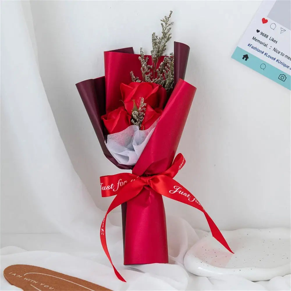 A vibrant red rose bouquet wrapped in glossy pink paper with a red ribbon and greenery.
