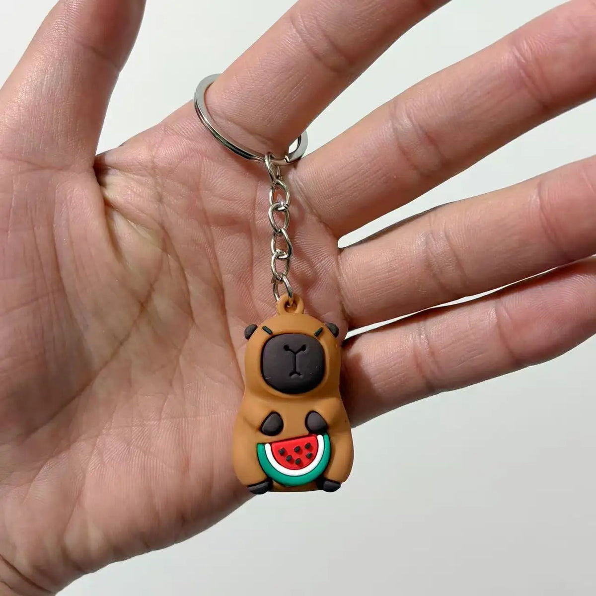 Un petit pendentif de clé en forme de capybara brun rond avec des détails noirs est tenu dans la main d'une personne.