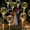 A couple stands in a dimly lit outdoor setting surrounded by glowing LED illuminated balloon spheres and string lights.