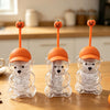 Three clear glass coffee cups shaped like bears with orange tops sitting on a wooden table.
