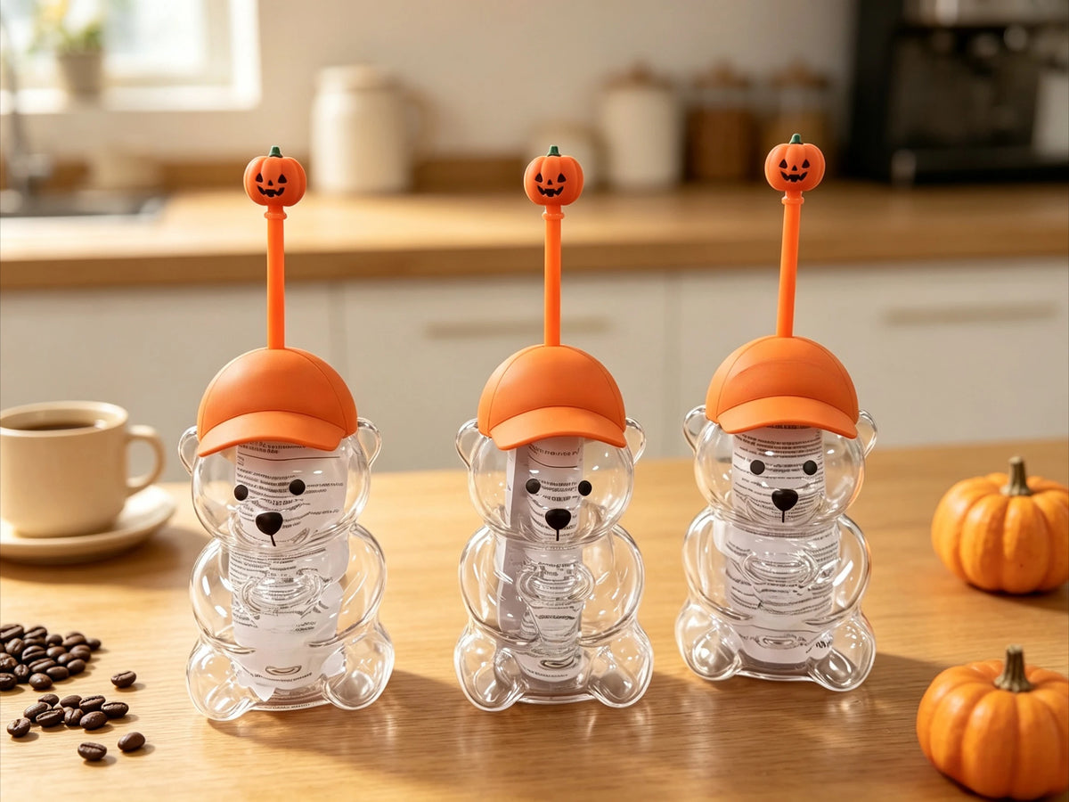 Three clear glass coffee cups shaped like bears with orange tops sitting on a wooden table.
