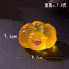 A round, yellow luminous resin ornament shaped like a smiling ghost face, with dimensions 1.6cm by 2.7cm.