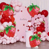 A display featuring pink and red balloons, including strawberry-shaped foil balloons and a cake.