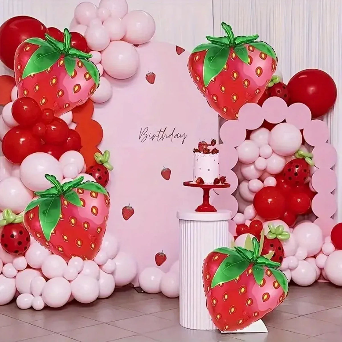 A display featuring pink and red balloons, including strawberry-shaped foil balloons and a cake.