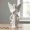 White gold praying angel figurine with outstretched wings and hands, standing on a wooden surface.