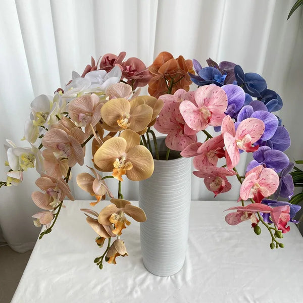 A bouquet of nine artificial butterfly orchids in shades of pink, peach, and purple arranged on a white table.