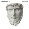 A white plaster bust miniature of a male face with curly hair and a beard.