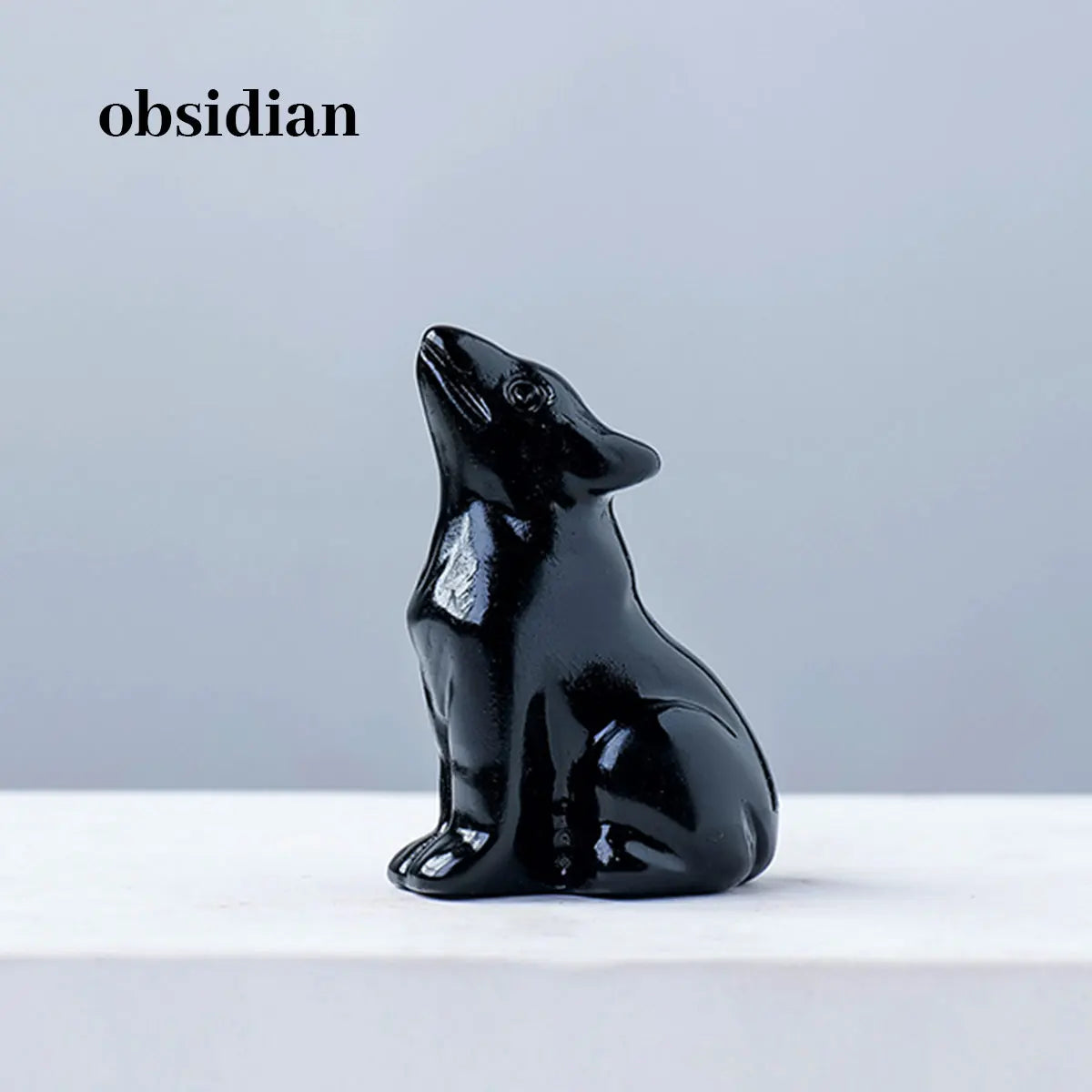 Schwarzes Obsidian-Schnitzwerk eines Wolfes, der auf einer weißen Oberfläche sitzt.