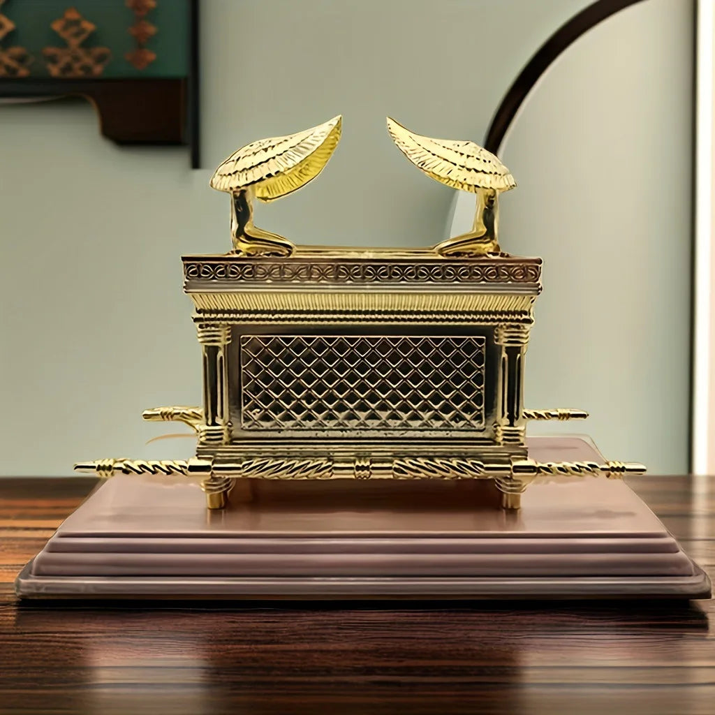 A golden metal statue of the Ark of the Covenant resting on a wooden surface.