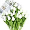 A bouquet of white artificial tulips with green leaves displayed on a white background.