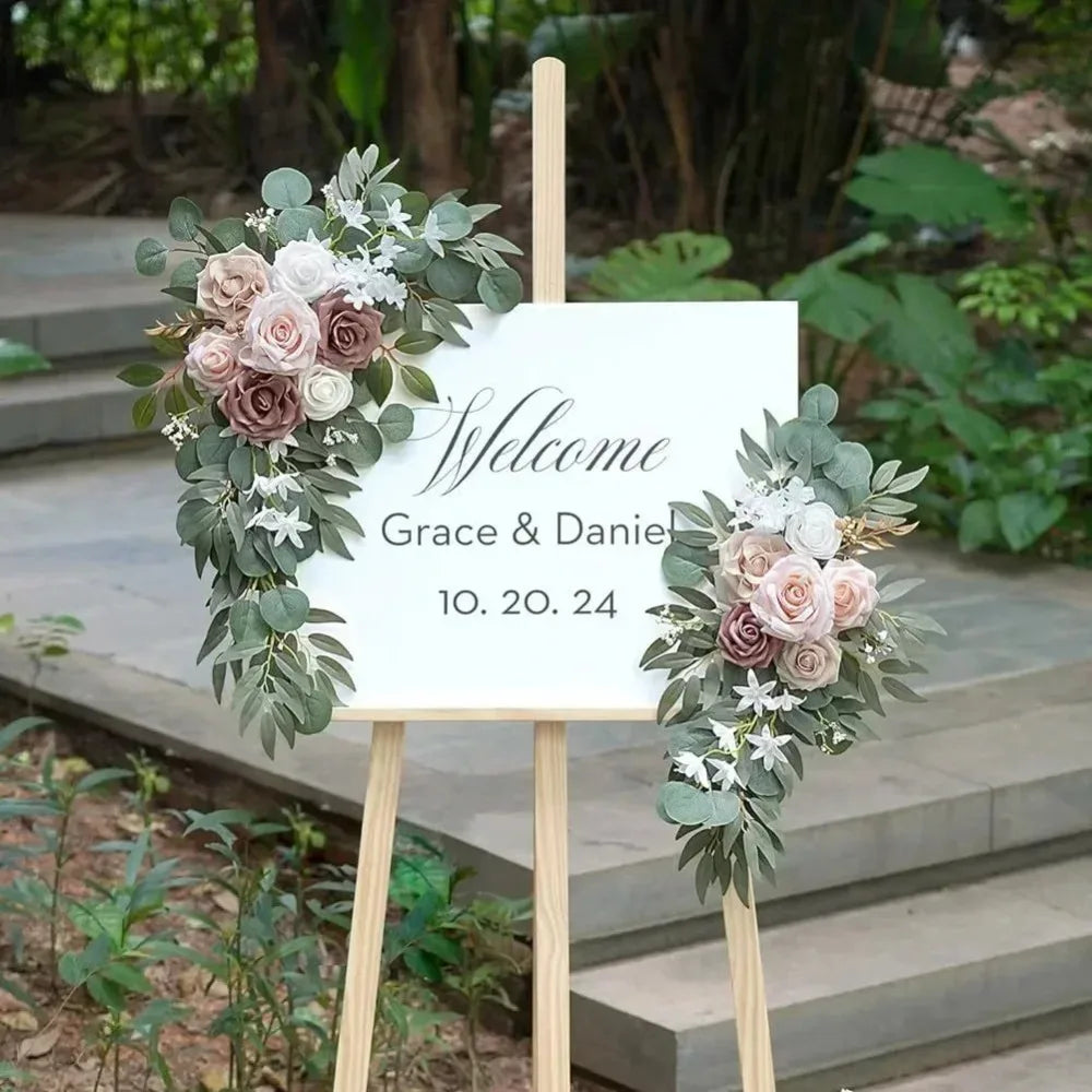 A wooden sign with 'Welcome Grace & Daniel 10.20.24' and floral arrangements featuring dusty rose and blue eucalyptus.