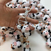 A hand holds a cluster of handmade crochet cow keychains featuring black and white patterns.