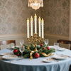 A centerpiece featuring six white taper candles in a brass candelabra on a light blue tablecloth.
