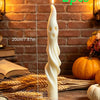 Two white soy candles shaped like a ghost and a mummy standing on straw in a rustic setting.