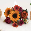 Un bouquet de tournesols artificiels et de pivoines rouges et oranges sur un tissu blanc.