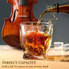 A glass of amber whiskey is being poured into a heavy base tumbler next to a wooden violin.