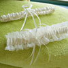 Ivory lace bowknot bridal garter set displayed on a textured lime green fabric.