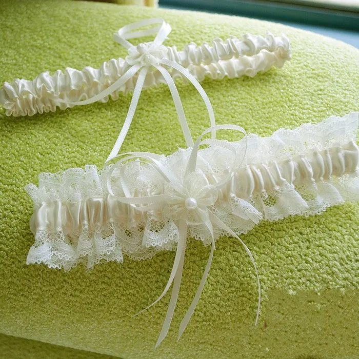 Ivory lace bowknot bridal garter set displayed on a textured lime green fabric.