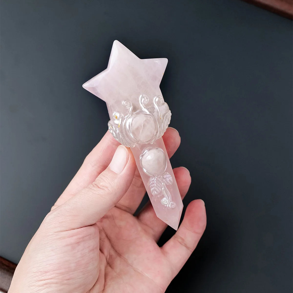 A hand holds a natural crystal moon and star scepter wand made of pink quartz.