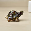 Glänzende, dunkelgrüne Kristall-Schildkrötenfigur mit goldenen Akzenten, auf neutralem Untergrund.
