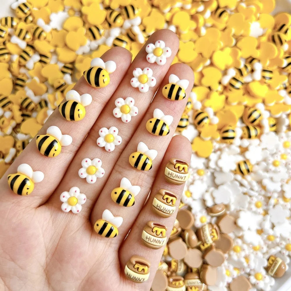 A hand displays a set of cute bee and daisy 3D resin nail art charms in various colors on a yellow background.