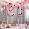 A large pink number balloon set featuring the number 1 with black bows, displayed in a soft light setting.