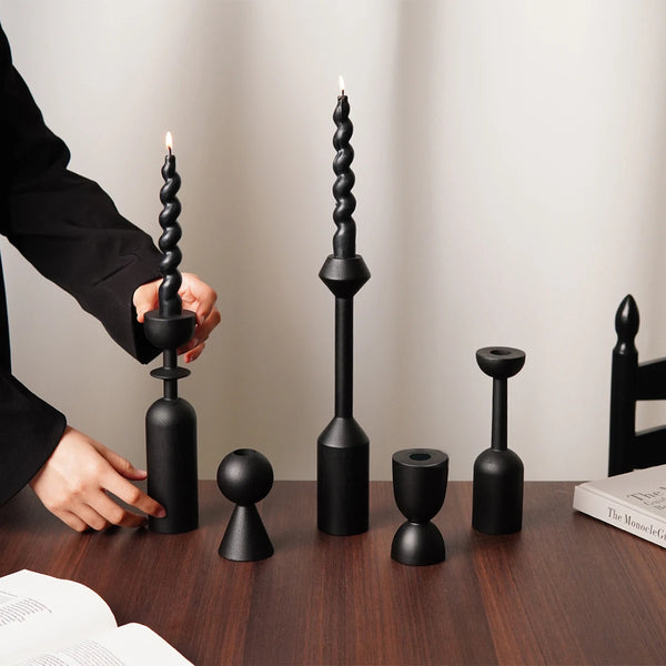 A set of two black vintage wooden candle holders or candlesticks with a lit candle on a dark wooden table.