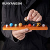 A hand holds a set of natural crystal solar system planet balls on a wooden tray.