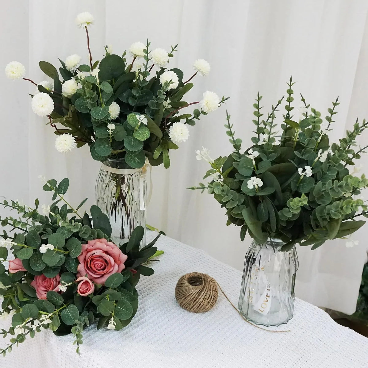 A floral arrangement featuring white flowers and green eucalyptus leaves displayed in glass vases.