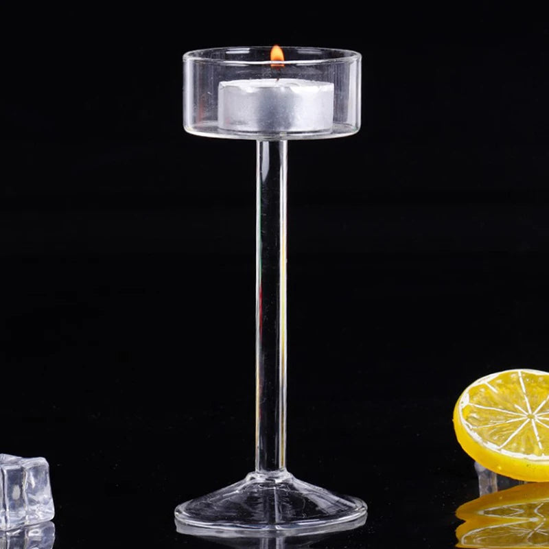 Elegant tall glass candle holder with a white candle burning on a black surface.