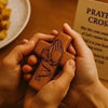 A pair of hands holds a handcrafted wooden prayer cross against a blurred background.