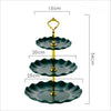 A three-tier plastic dessert stand with dark green scalloped plates and a gold-colored serving fork.