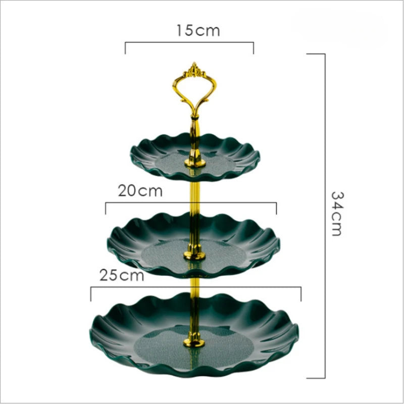 A three-tier plastic dessert stand with dark green scalloped plates and a gold-colored serving fork.