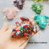 A hand holds a colorful resin crystal frog decoration next to several other frogs on a gray surface.