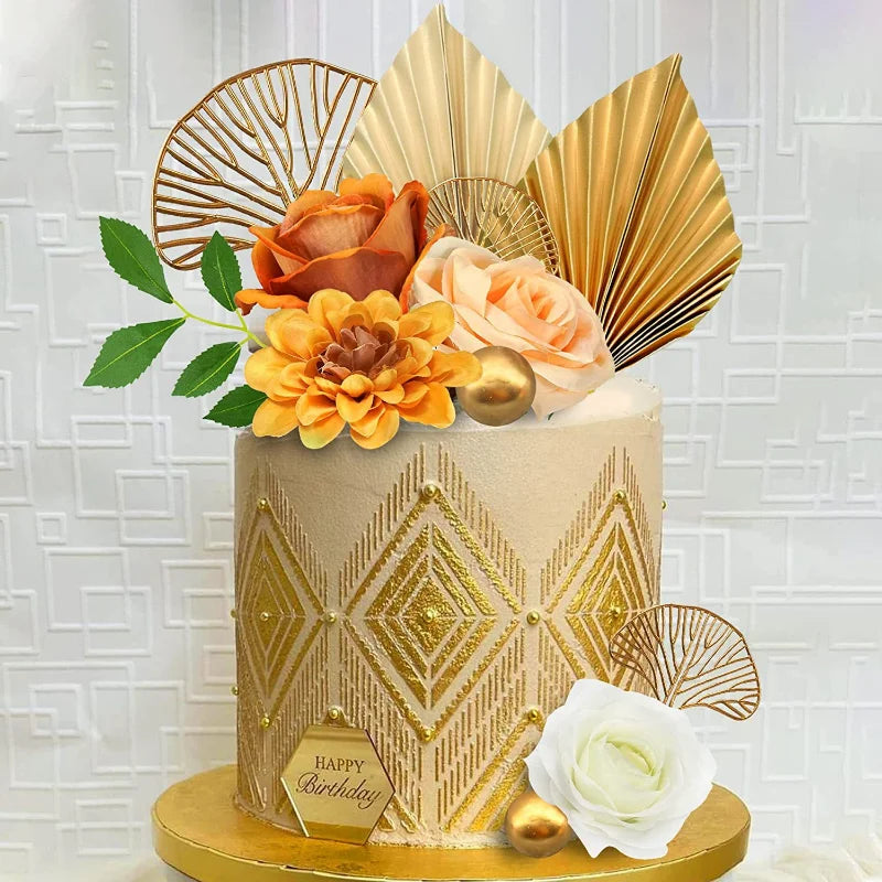 A tiered cake decorated with gold leaf accents, palm leaf cutouts, and orange and peach roses.