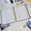 An open linen cover photo album displaying blank pages and decorative twine on a white textured surface.