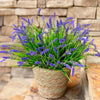 A potted artificial lavender plant with purple flowers sits on a stone surface.