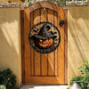 Panneau de décoration d'Halloween rond en bois avec visage de citrouille sculptée suspendu sur une porte rustique.