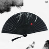 A black hand carved bamboo folding fan with white leaf designs and a small bird detail.