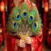 Une personne tient un éventail de plumes de paon naturel avec des plumes vertes et bleues irisées contre un vêtement rouge.