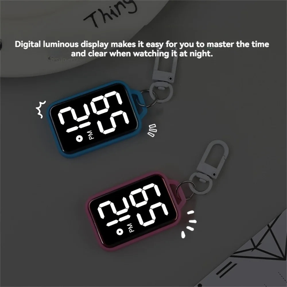 A digital luminous display keychain pocket watch in blue and pink colors resting on a gray surface.
