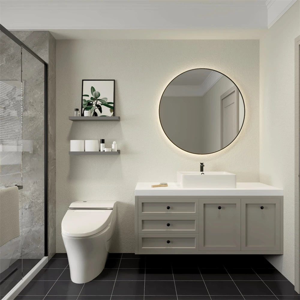 A modern bathroom featuring a white vanity, circular mirror, and toilet against a light wall with dark floor tiles.