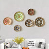 A collection of nine round bohemian straw wall decor hanging in various shades of natural and earthy tones.