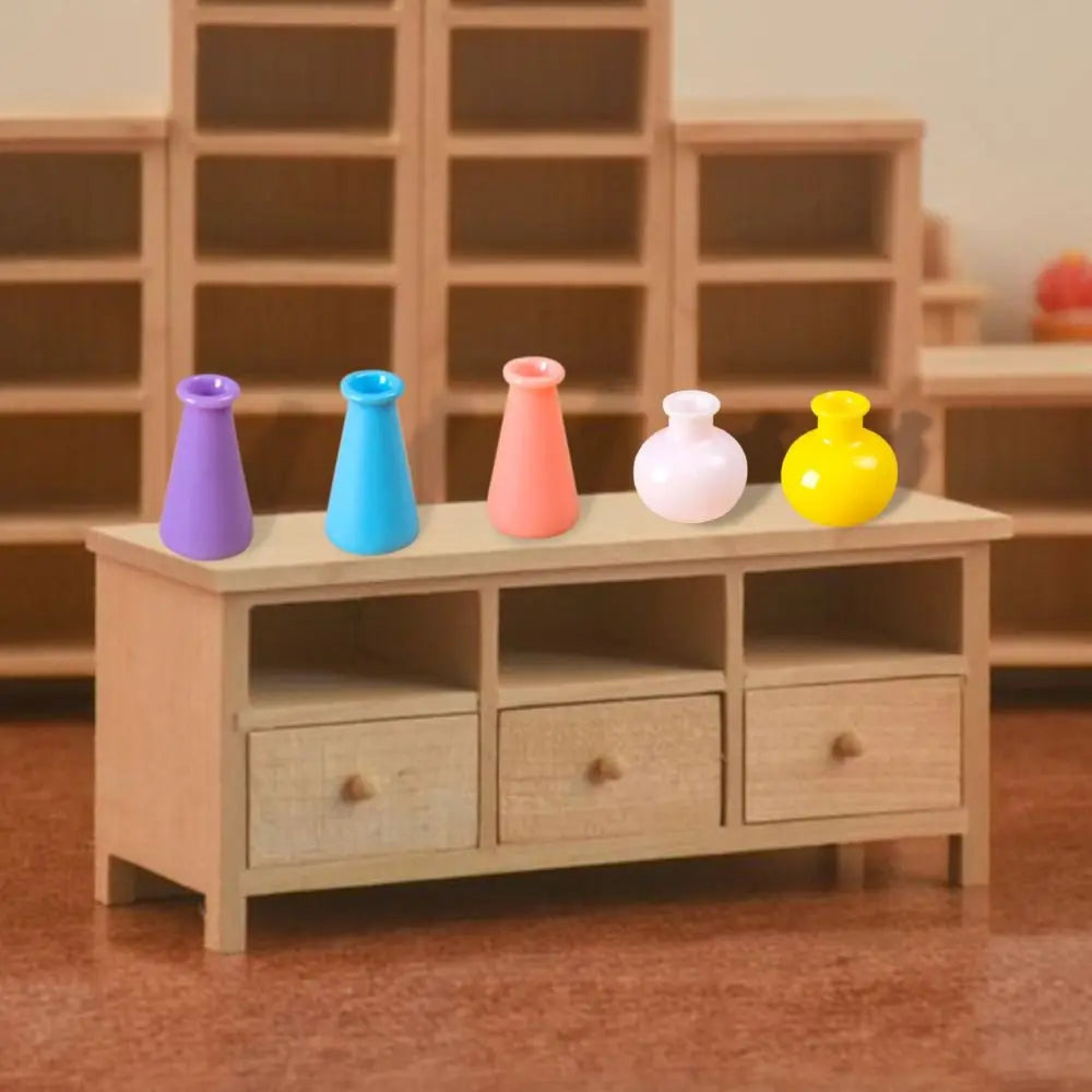 A collection of five miniature resin vases in purple, blue, pink, white, and yellow displayed on a wooden shelf.