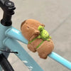 A small, brown capybara animal charm is attached to a light blue bicycle frame.