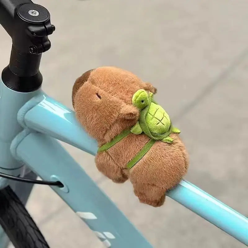 A small, brown capybara animal charm is attached to a light blue bicycle frame.